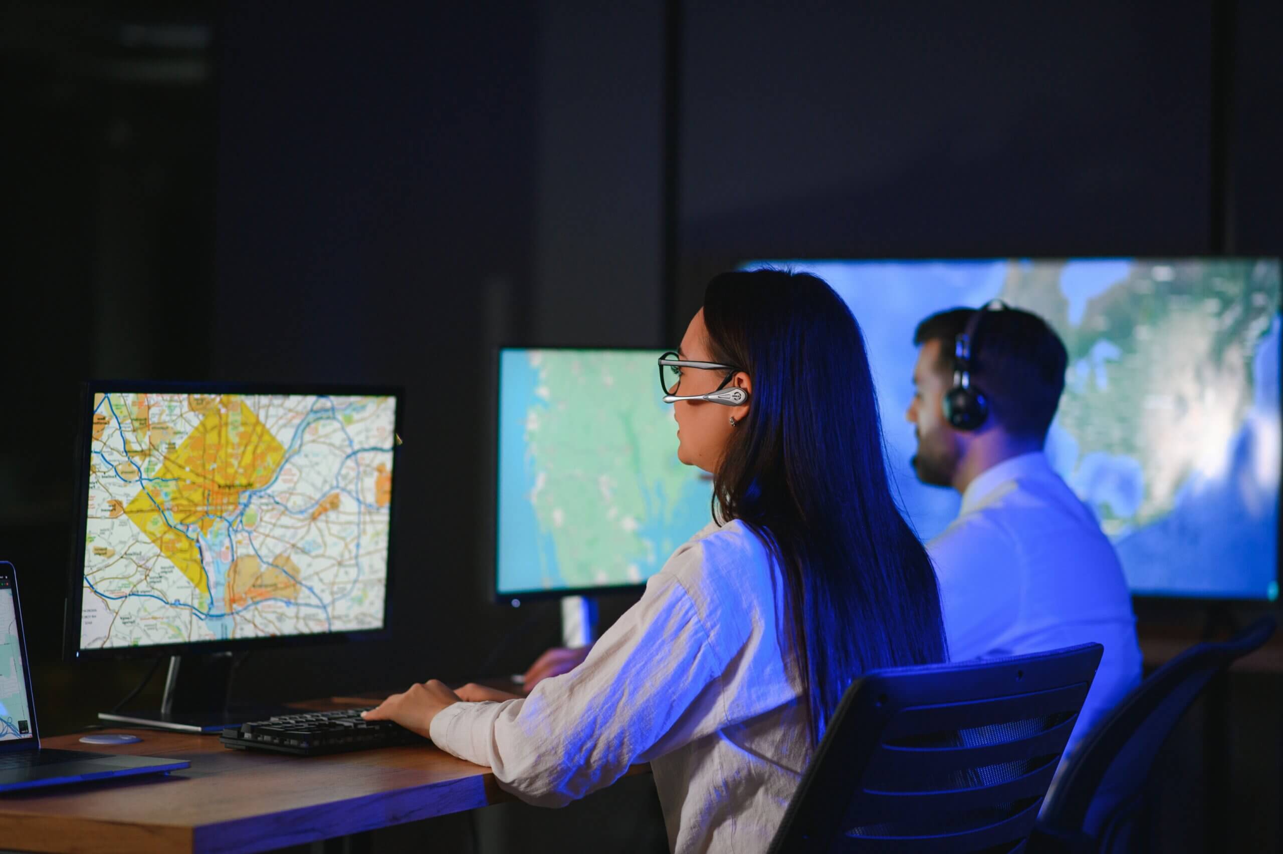 Two people analyze geospatial data on computers. Maps, data types, and file formats displayed.